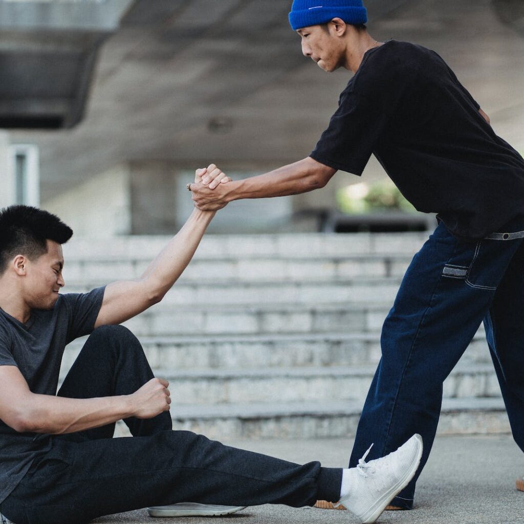 Asian man helping friend to get up from ground