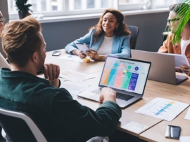 Positive multiethnic casually dressed colleagues sitting at conference table with laptops and documents and discussing business issues in modern workspace