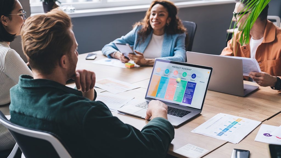 Positive multiethnic casually dressed colleagues sitting at conference table with laptops and documents and discussing business issues in modern workspace