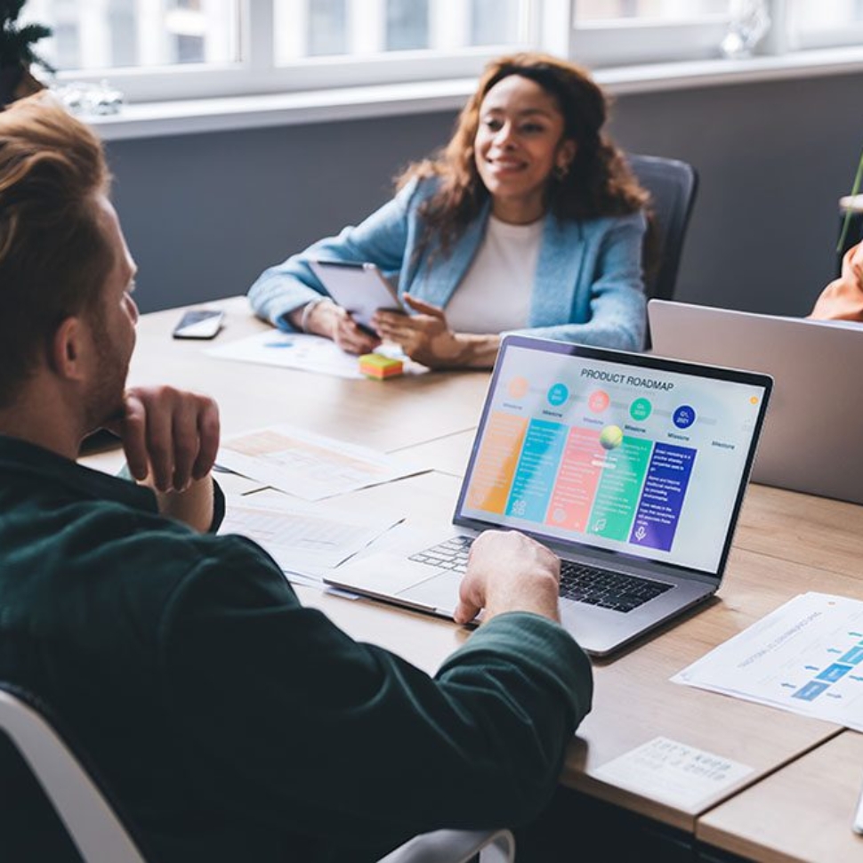 Positive multiethnic casually dressed colleagues sitting at conference table with laptops and documents and discussing business issues in modern workspace