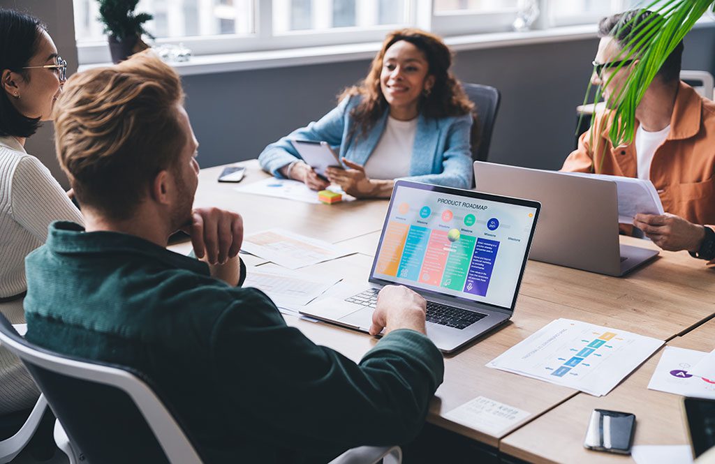 Positive multiethnic casually dressed colleagues sitting at conference table with laptops and documents and discussing business issues in modern workspace