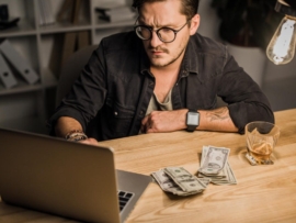 Case Studies 33 young man with whiskey and pile of cash using laptop