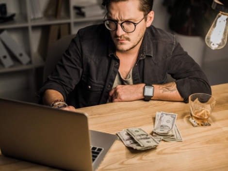 SEO Services 33 young man with whiskey and pile of cash using laptop