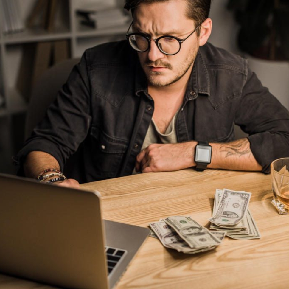 young man with whiskey and pile of cash using laptop